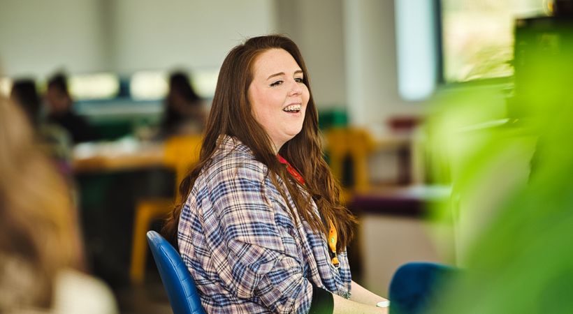 PSS teammate is sat on a chair, she is smiling and laughing.