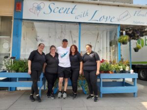 Paul stands between four of the team members at Scent With Love florist. They are huddled up close and Paul has his arms around them