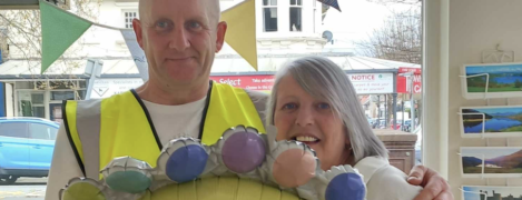 Paul holds a sunshine shaped balloon with one hand and hugs Shared lives carer Andrea with his other arm. They smile at the camera.