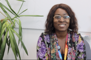 Lisa is a Black women, with shoulder length brown hair. She wears wide framed glasses and a colourful top. She smiles during an interview she filmed with PSS.